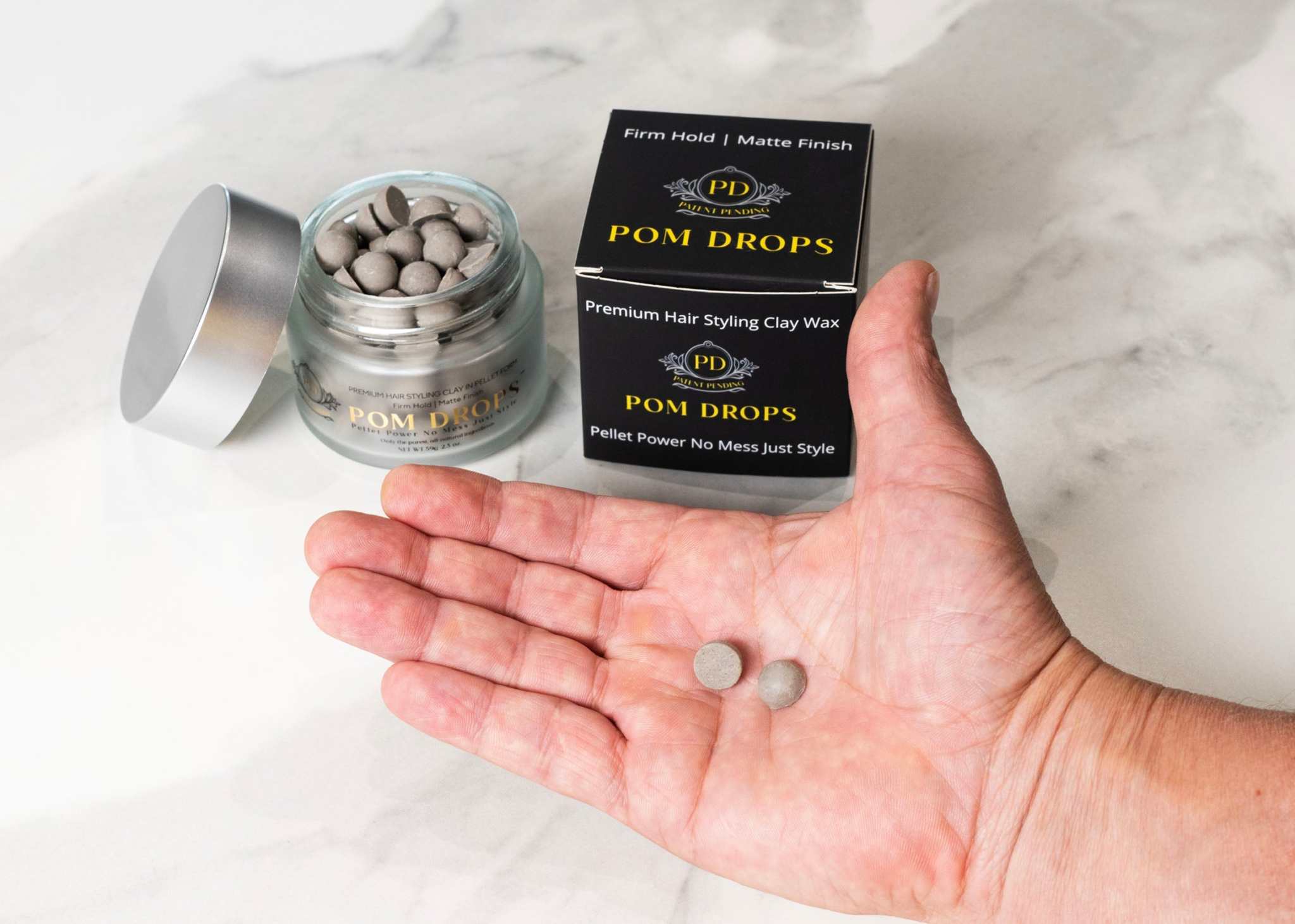 Close-up of POM DROPS hair styling clay pellet resting in palm of hand